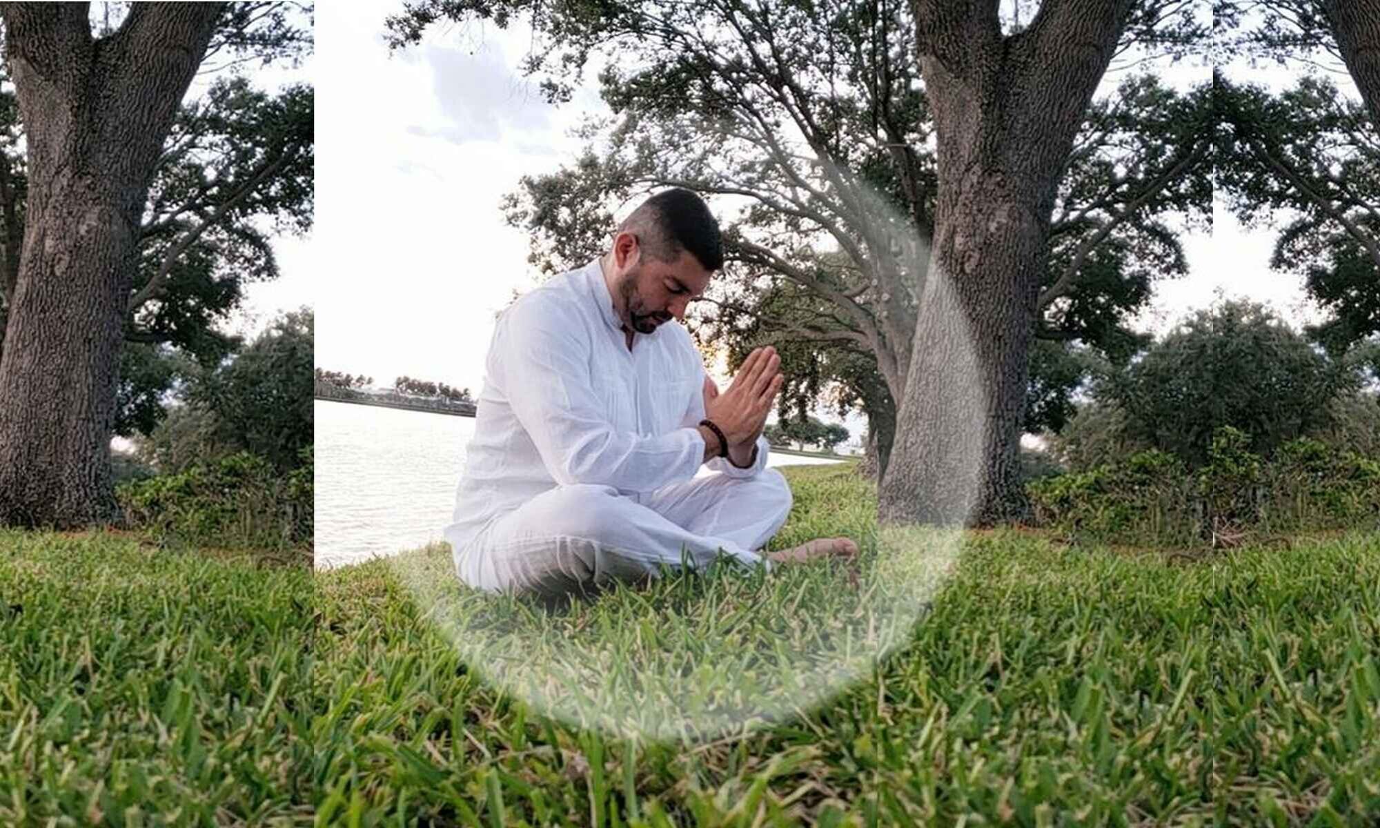 Hombre vestido de blanco en posición de meditación y oración en la naturaleza para sanación espiritual por el curandero blanco.